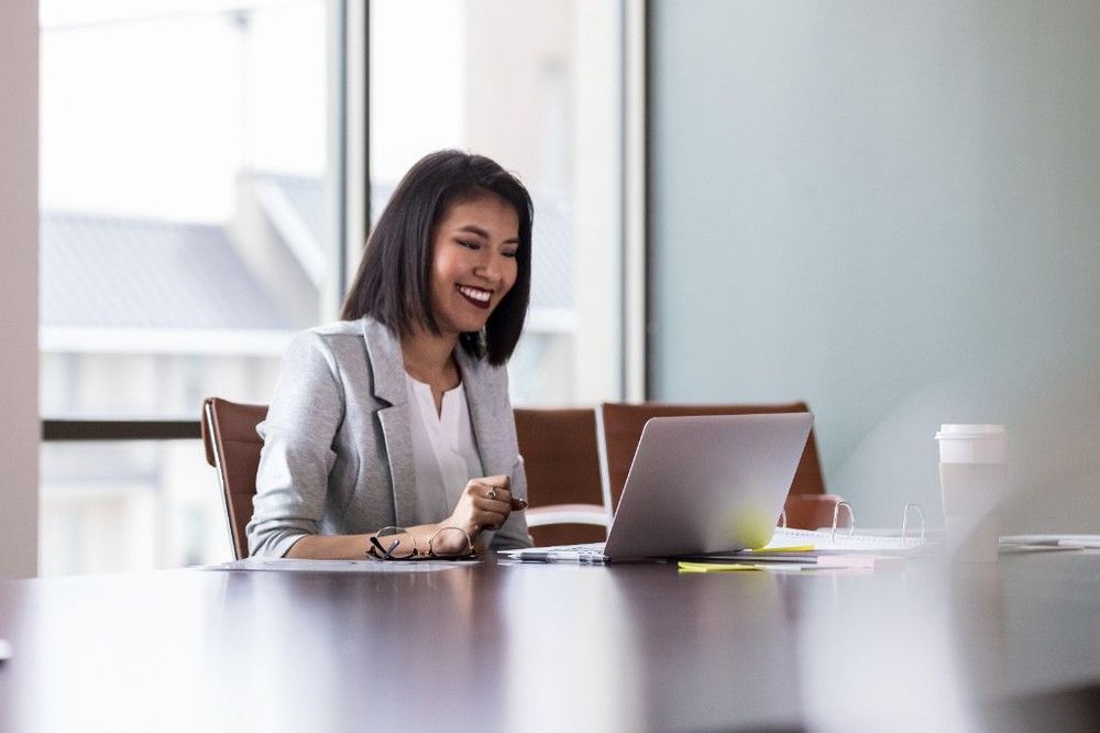 A young professional smiling while working on a laptop in a conference room