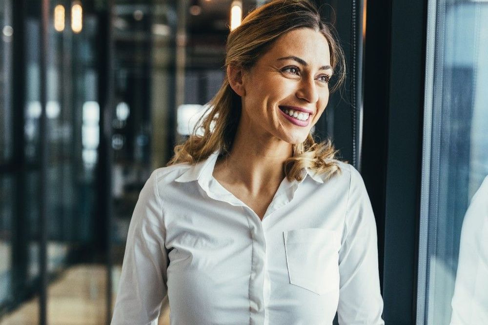 A smiling professional woman in a white shirt standing in a modern office