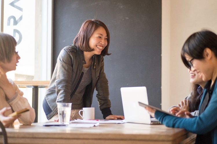 Asian American professionals collaborating around a laptop at a café table