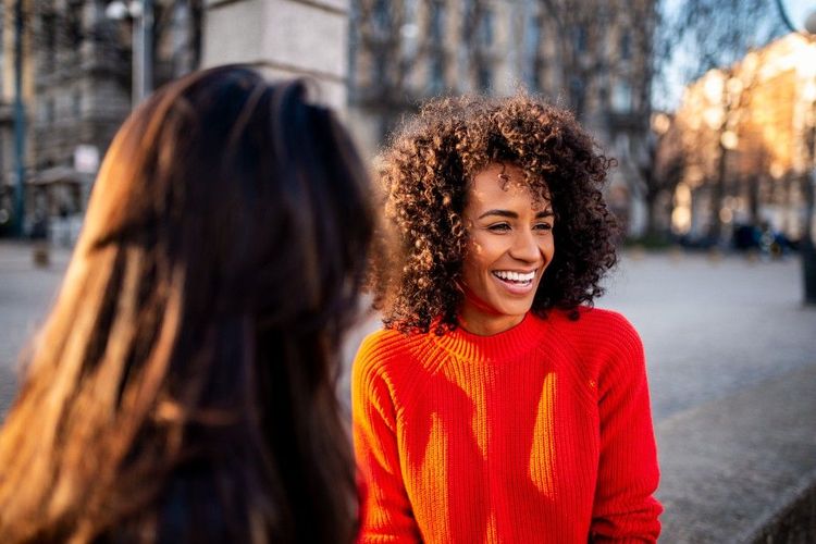 A woman laughing with a friend outdoors in a sunny city plaza
