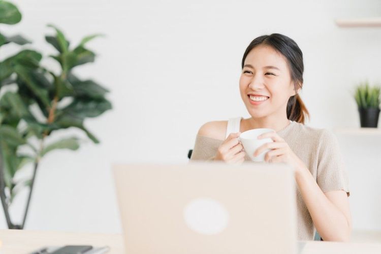 A young professional smiling with a coffee mug at a laptop desk